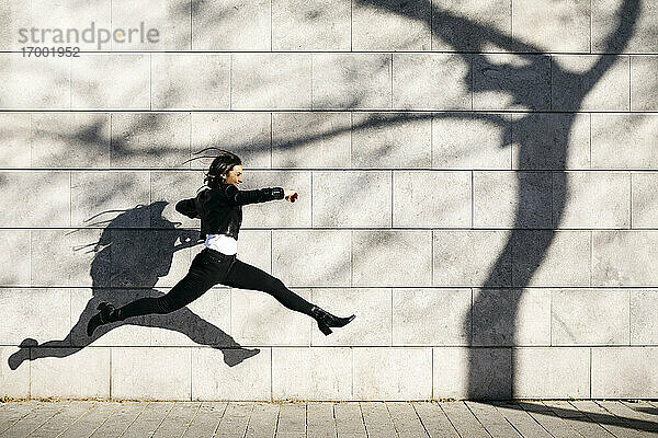 Junge Frau macht einen großen Sprung auf einer Mauer mit einem Schatten eines Baumes