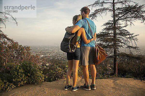 Paar  das sich umarmt  während es auf einem Berg stehend die Aussicht betrachtet