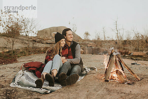 Junges Paar sitzt zusammen vor einem Lagerfeuer