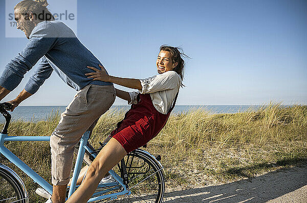 Glückliche Frau genießt Fahrradfahrt mit Mann gegen klaren Himmel