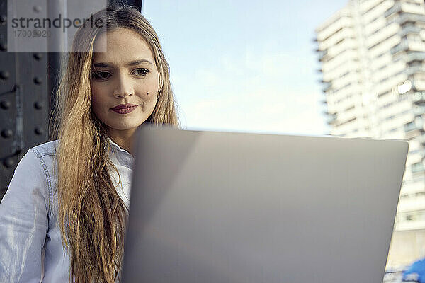 Junge Geschäftsfrau  die einen Laptop benutzt  während sie im Freien sitzt
