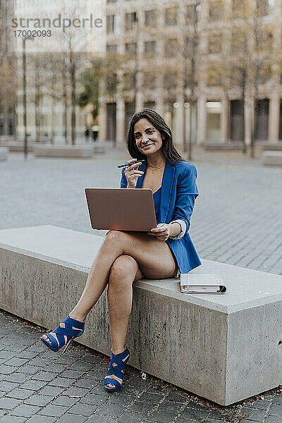 Lächelnde Unternehmerin mit Laptop auf einer Bank in der Stadt sitzend