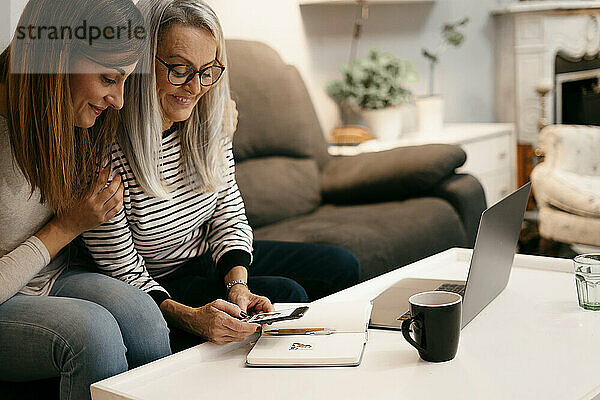 Lächelnde Mutter und Tochter  die ein Foto auf einem Buch über ein Mobiltelefon machen  während sie zu Hause sitzen