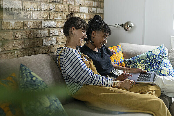 Lesbisches Paar  das lächelnd einen Laptop benutzt und zu Hause auf dem Sofa sitzt