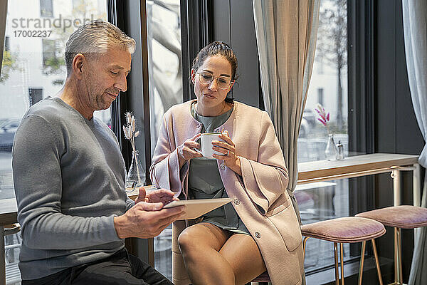 Geschäftsleute arbeiten an einem digitalen Tablet  während sie in einem modernen Cafe sitzen