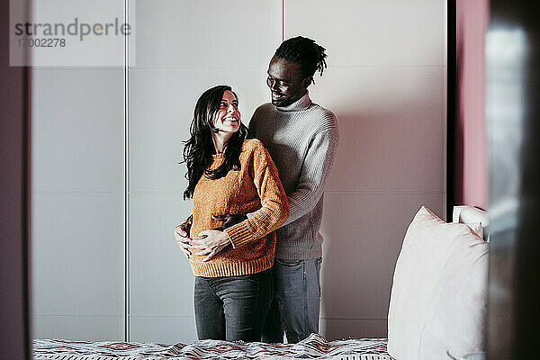 Glücklicher Mann umarmt schwangere Frau im Schlafzimmer zu Hause