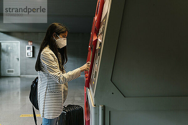 Frau mit Gesichtsmaske beim Kauf eines Zugtickets am Kiosk während COVID-19