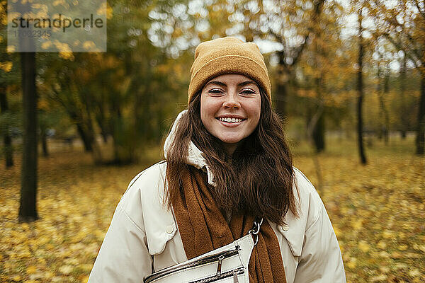 Glückliche junge Frau in warmer Kleidung im herbstlichen Park