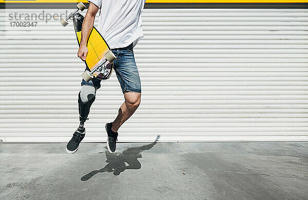 Junger Mann mit Beinprothese hält Skateboard und springt