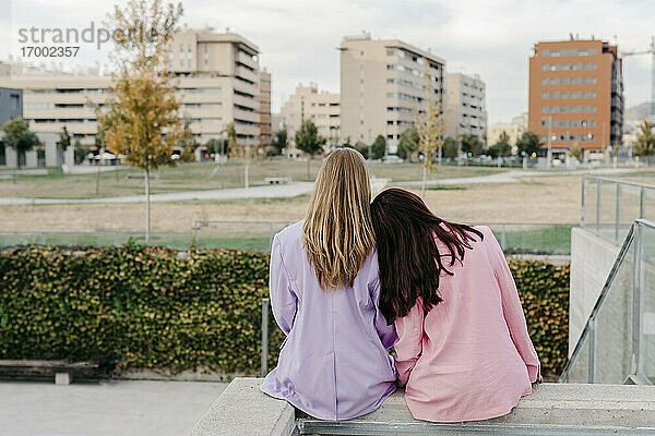 Frau stützt sich auf die Schulter ihrer Schwester  während sie auf einem Dach gegen den Himmel in der Stadt sitzt