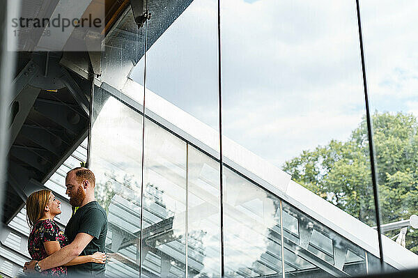 Heterosexuelles Paar umarmt sich vor einem Glasfenster