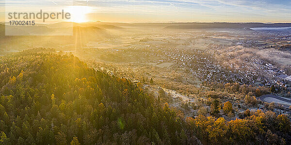 Drone Blick auf Herbst Wald bei nebligen Sonnenaufgang mit Dorf im Hintergrund