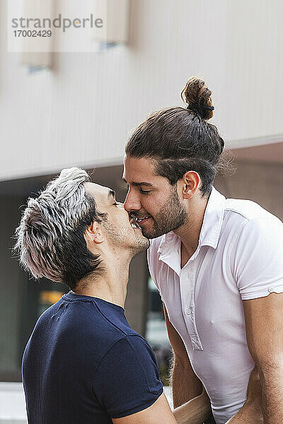 Lächelndes schwules Paar küsst sich vor einem Gebäude in der Stadt