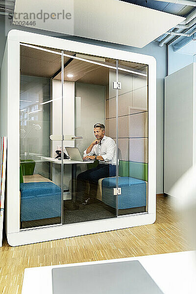 Geschäftsmann arbeitet am Laptop  während er in einer Kabine im Büro sitzt