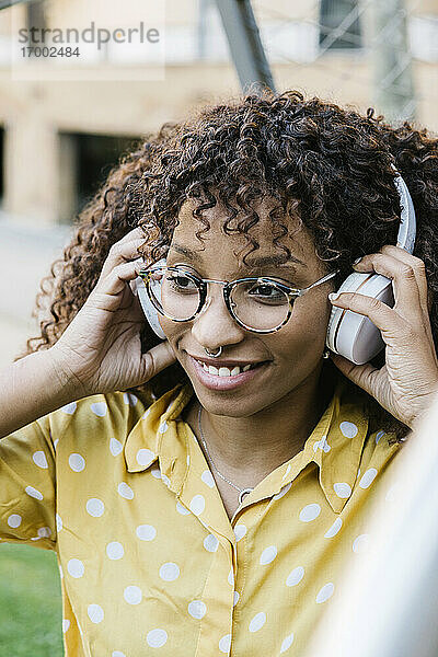 Lächelnde Frau mit Kopfhörern  die Musik hört  während sie im Freien steht