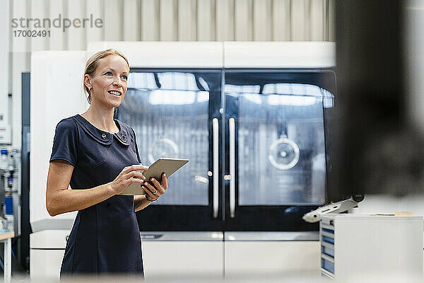 Lächelnde Geschäftsfrau  die ein digitales Tablet hält  während sie in einer Fabrik steht