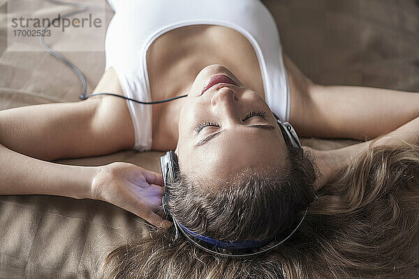 Nahaufnahme einer Frau  die beim Entspannen auf dem Bett über Kopfhörer Musik hört