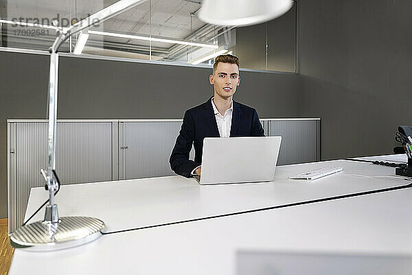 Junger Geschäftsmann mit Laptop im Büro sitzend