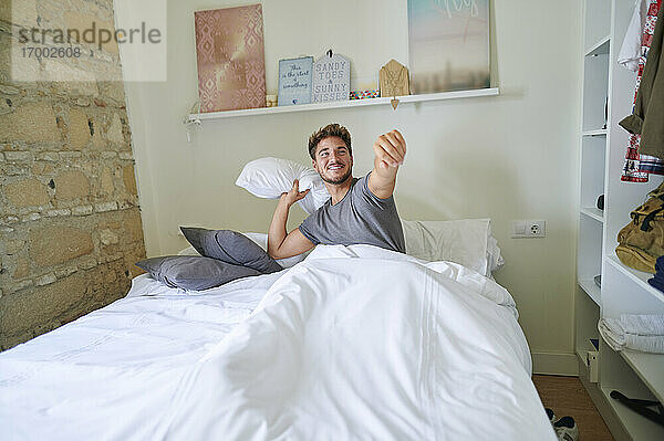 Verspielter Mann spielt mit Kissen im Schlafzimmer zu Hause