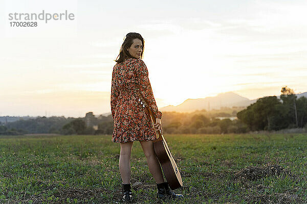 Junge Frau mit Gitarre auf einer Wiese bei Sonnenuntergang