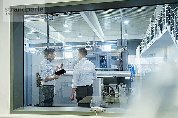 Männliche Kollegen mit digitalem Tablet  die über Maschinen in einer Fabrik diskutieren