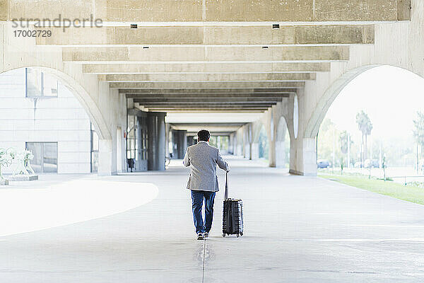 Älterer Geschäftsmann mit Gepäck auf einem betonierten Fußweg