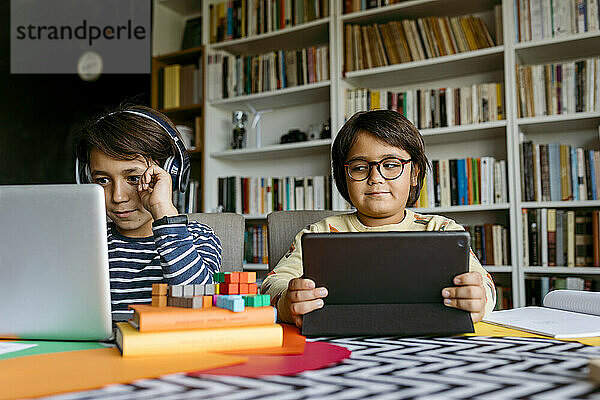 Lächelnder Junge beim E-Learning am Laptop  während ein männlicher Freund zu Hause zuschaut