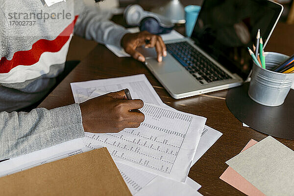 Männlicher Finanzberater  der zu Hause am Laptop eine Strichliste auf Papier erstellt
