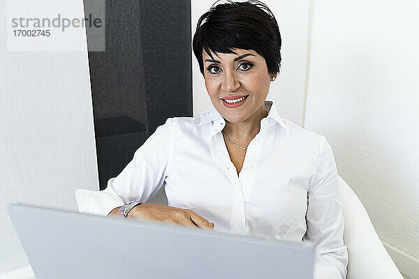 Porträt einer Geschäftsfrau  die in die Kamera lächelt  während sie mit einem Laptop sitzt