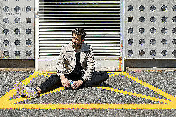 Hilfloser Mann sitzt auf dem Boden im gelb markierten Bereich vor einer Betonmauer