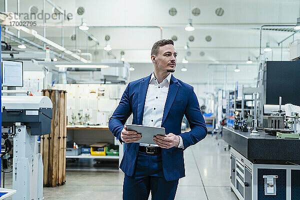 Geschäftsmann hält digitales Tablet  während er sich in einer Fabrik umsieht