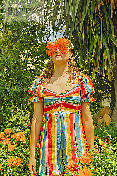 Porträt einer Frau in der Natur mit Brille und orangefarbenen Blumen  die ihre Augen bedecken