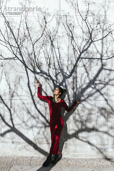 Frau in rotem Kleid mit Tänzerin Pose und Baum Schatten an der Wand