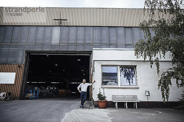 Männlicher Unternehmer  der sich an eine Kabine lehnt  während er am Eingang der Fabrik steht