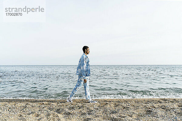 Junger Mann in Jeans-Outfit läuft gegen das Meer