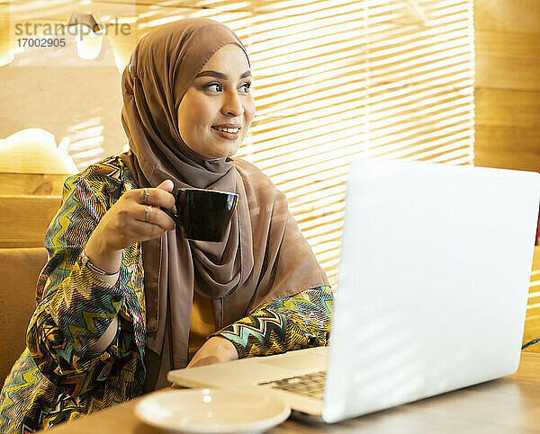 Frau trägt Hijab und trinkt Kaffee  während sie im Cafe sitzt