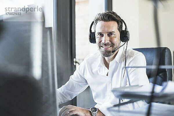 Lächelnder Geschäftsmann mit Kopfhörern  der im Büro sitzt