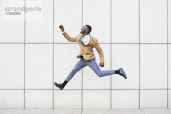 Junger Geschäftsmann springt und macht ein Selfie vor einer Mauer