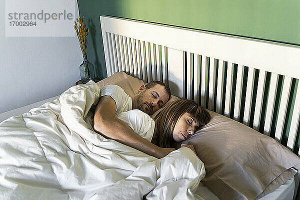 Mid adult couple sleeping together on bed at home