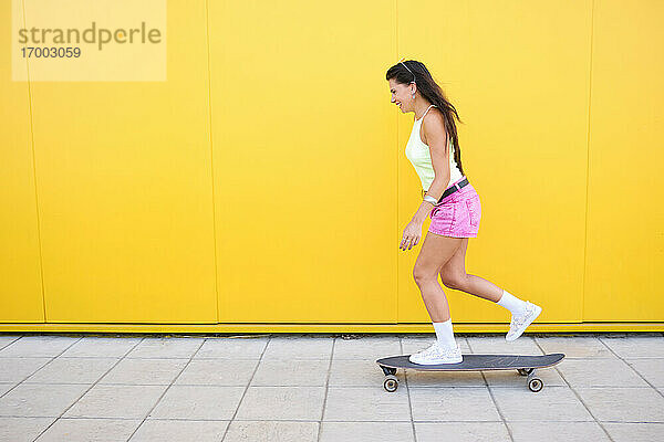 Schönes Mädchen skateboarding entlang gelbe Wand im Sommer