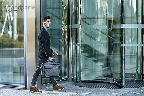 Junger Geschäftsmann mit Aktentasche auf dem Weg zu einem Bürogebäude