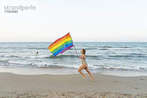 Ältere Frau läuft am Strand mit Homosexuell Stolz Flagge
