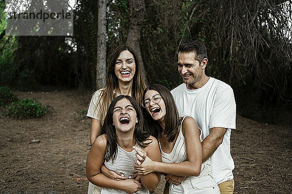 Eltern mit Töchtern  die lachend im Wald stehen  während sie im Urlaub sind
