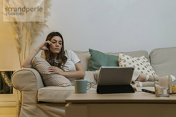 Junge Frau mit digitalem Tablet entspannt sich auf dem Sofa zu Hause