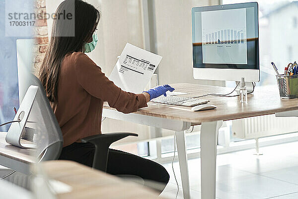 Geschäftsfrau bei der Arbeit an einem Bericht im Computer am Arbeitsplatz während COVID-19