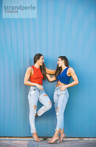 Lächelnde Zwillinge lehnen an einer blauen Wand