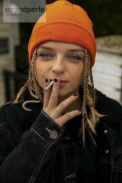 Modische junge Frau mit blauen Augen raucht Zigarette