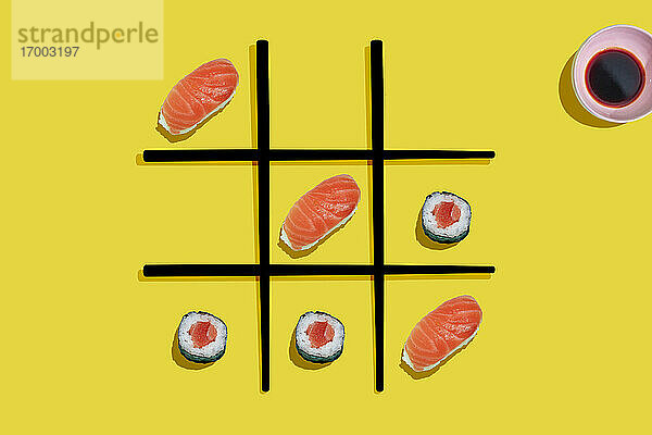 Tic-Tac-Toe-Spiel mit Lachs-Sushi Maki und Nigiri mit schwarzen Essstäbchen auf gelbem Hintergrund