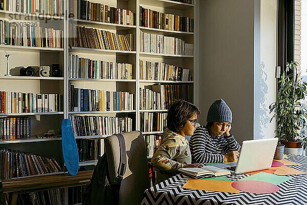 Jungen  die im Wohnzimmer sitzend mit dem Laptop konzentriert e-Learning betreiben