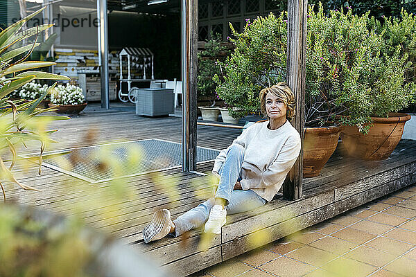 Blonde Frau  die auf dem Holzboden eines Dachgartens sitzt und nachdenkt